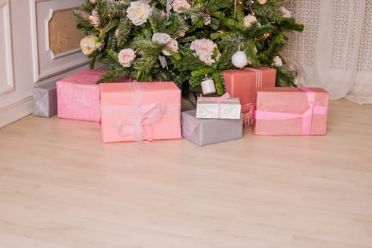 Great beautifully decorated Christmas tree with pink baubles, ribbons, snowflakes, and a lot of gift boxes and toys beneath. Over white brick background
