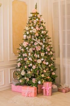 Pastel christmas.pinkChristmas gift box with golden ribbon next to decorated Christmas tree