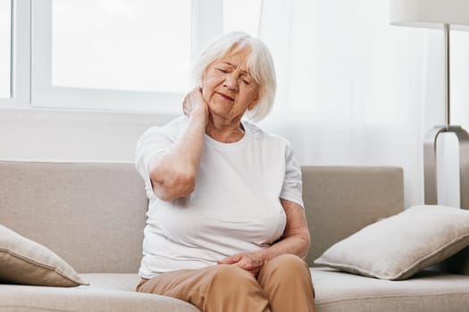 Elderly woman severe neck pain sitting on the sofa, health problems in old age, poor quality of life. High quality photo