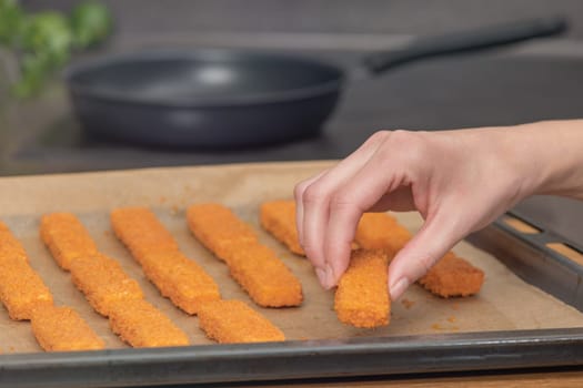 The hand lays out fish fingers against the background of a frying pan on special paper. The concept of frying fish sticks in the oven. Side view. High quality photo