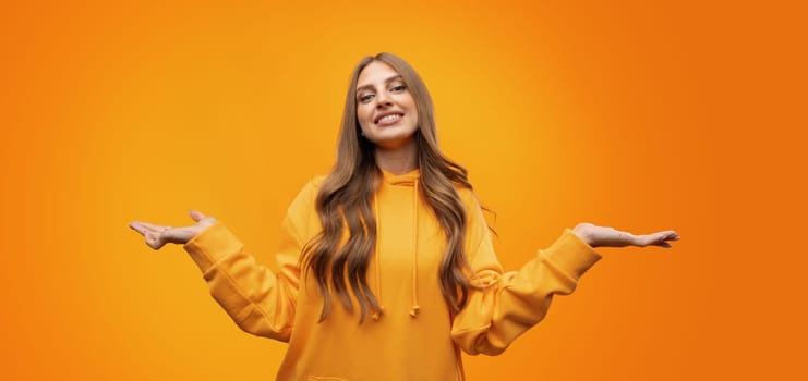 Portrait of cute attractive young woman showing whatever gesture on yellow background in studio