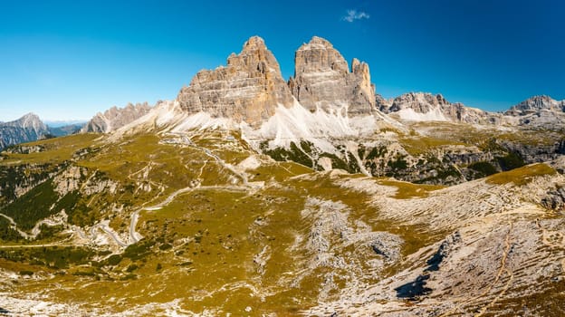 Mountainous terrain at sunrise. Majestic Three Peaks of Lavaredo with sand-covered foothills in Alps at beginning of sunny day aerial view in back lit