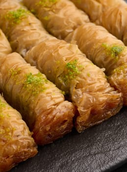 Pieces of baked baklava in honey and sprinkled with pistachios on a black board