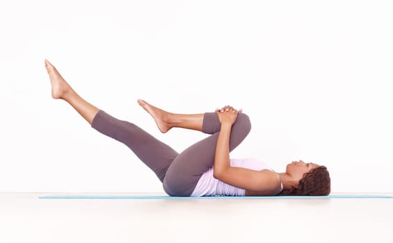 Yoga, leg stretch and black woman in studio on a fitness and workout mat for training. Isolated, white background and African female person lying on the ground with sport stretching for wellness.