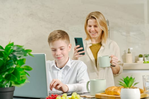 Happy mother and son have healthy breakfast in the kitchen at home. Happy mother and son in the kitchen. breakfast and digital devices Concept of happy family and healthy food.