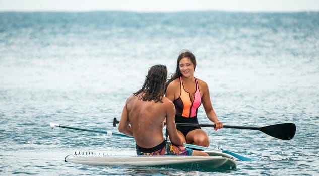 Sea woman and man on sup. Silhouette of happy young woman and man, surfing on SUP board, confident paddling through water surface. Idyllic sunset. Active lifestyle at sea or river