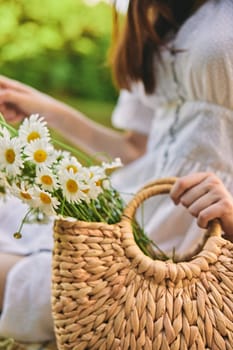 close vertical photo of a woman's hands with a wicker bag with daisies. High quality photo