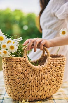 close vertical photo of a woman's hands with a wicker bag with daisies. High quality photo