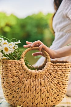 close vertical photo of a woman's hands with a wicker bag with daisies. High quality photo