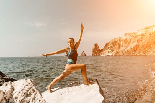 Yoga on the beach. A happy woman meditating in a yoga pose on the beach, surrounded by the ocean and rock mountains, promoting a healthy lifestyle outdoors in nature, and inspiring fitness concept