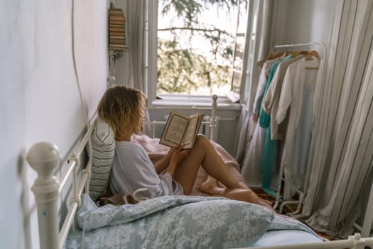 Woman reading a book in bed, lying on her stomach smiling happy and relaxed on a leisure day at home.