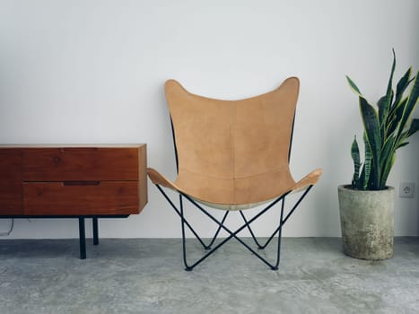 Stylish leather chair chair in a modern interior with white walls and concrete floor, wooden elements, natural daylight from the window. High quality photo