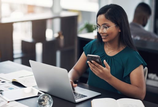 Technology helps bring her designs to life. a young designer using a laptop and cellphone in an office