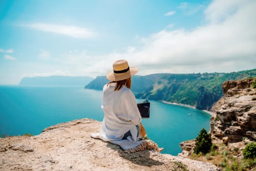 Freelance woman working on a laptop by the sea, typing away on the keyboard while enjoying the beautiful view, highlighting the idea of remote work