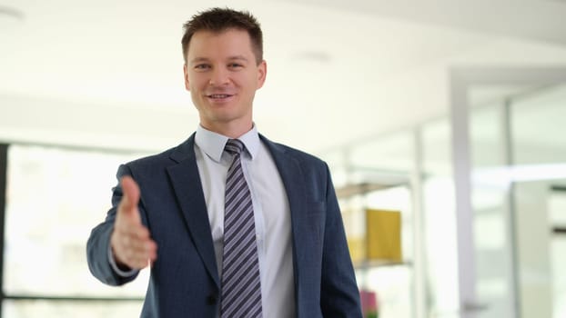 Businessman in suit with tie extending hand for handshake in office. Business partnership and teamwork concept