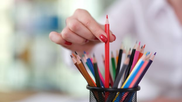 Female hand taking out red pencil from glass closeup. Office stationery concept