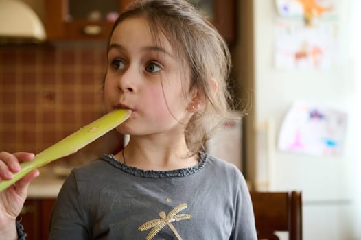 Close-up portrait of adorable little child girl licking a utensil with sweet cake chocolate cream, looking slyly away. Happy childhood and children concept. People. Family. Cooking. Leisure activity