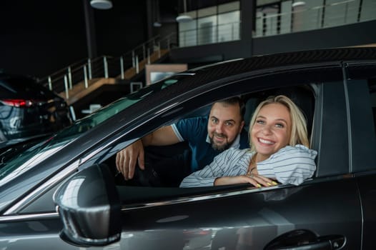 Happy caucasian couple is sitting in a new car in a car dealership
