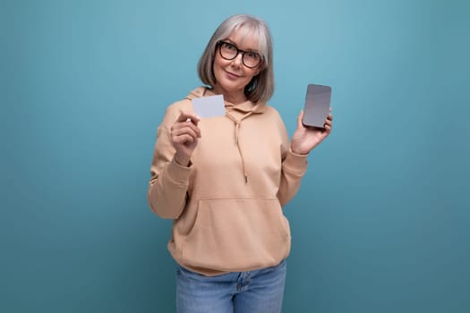 60s granny woman with gray hair keeps her savings on a credit card on a studio background with copy space.