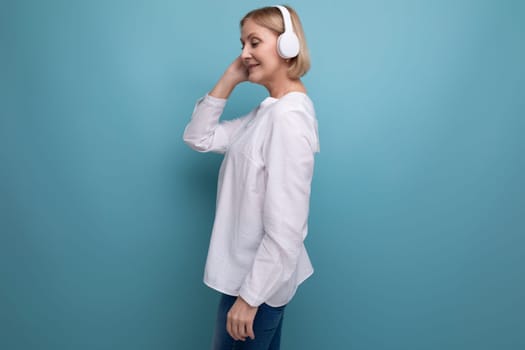 50s woman with blonde hair dancing to music in wireless headphones.