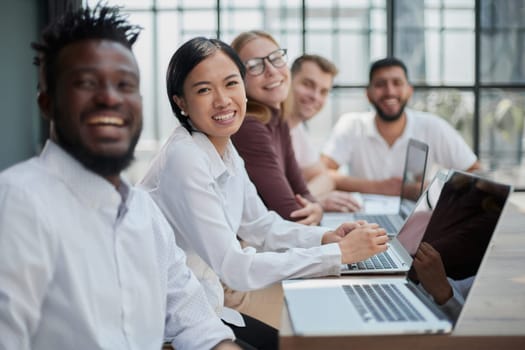 Multicultural colleagues sitting at desk near digital devices and documents during business meeting