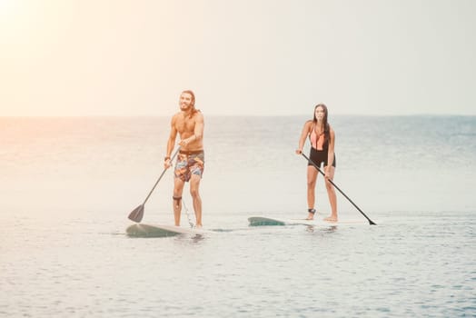 Sea woman and man on sup. Silhouette of happy young woman and man, surfing on SUP board, confident paddling through water surface. Idyllic sunset. Active lifestyle at sea or river