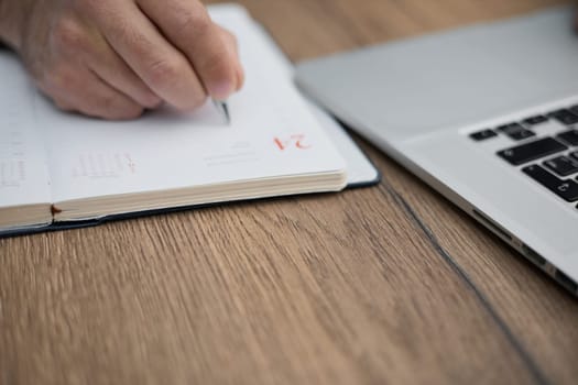 Hands writes a pen in a notebook, computer keyboard in background