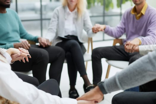 Diverse people sitting in circle holding hands at group therapy