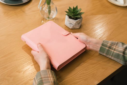 Close up picture of woman hands holding pink mockup notebook. Girl holding a pink blank space notepad with small cactus on the table. Mockup blank copy space notepad.