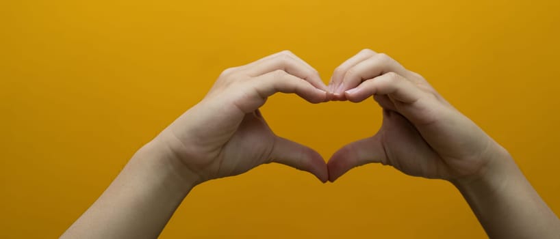 Unrecognizable making heart with hands isolated on yellow background. Love, Valentine's day, sign, symbol concept.