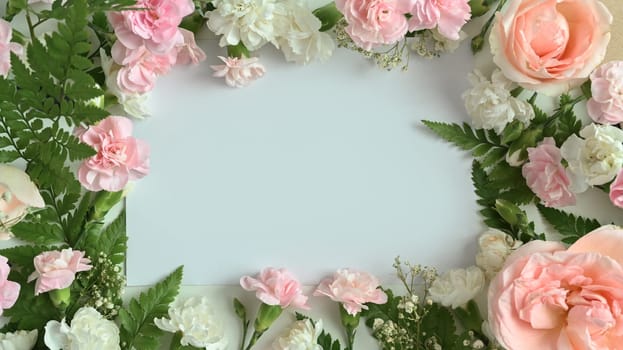 Frame made of pink rose, carnation and fern leaves on white background. Flat lay, top view with space for text.