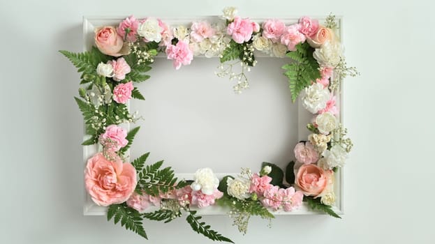 Round frame made of pink rose, carnation and fern leaves on white background. Spring floral background, copy space.