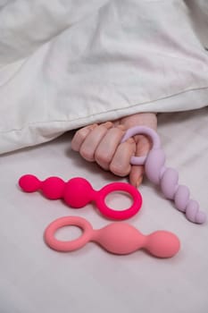 A woman chooses anal beads from a set while lying in bed