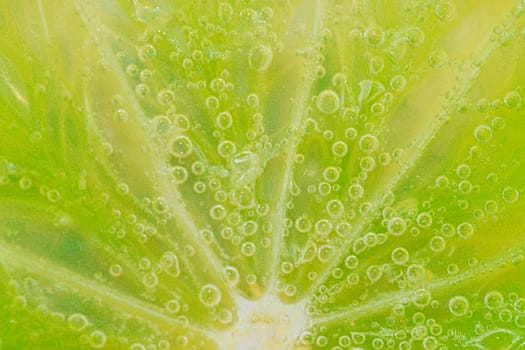 Slice of ripe lime in water. Close-up of lime in liquid with bubbles. Slice of ripe lime in sparkling water. Macro horizontal image of fruit in carbonated water