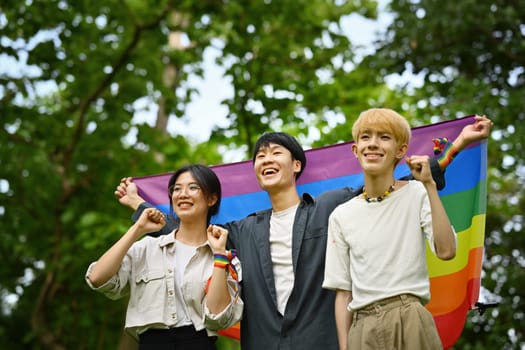 Group of young people holding pride rainbow flag, supporting LGBTQ community and equality social.