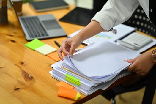 Cropped shot of female accountant working with annual financial report, preparing present at wooden office desk.