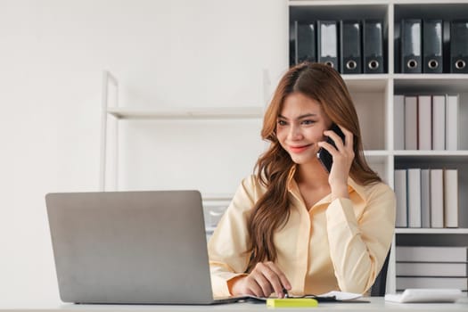 Portrait of financial business woman sitting at desk and working on laptop while making talk on the phone.