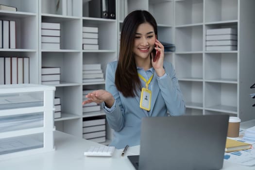 Portrait of financial business woman sitting at desk and working on laptop while making talk on the phone.