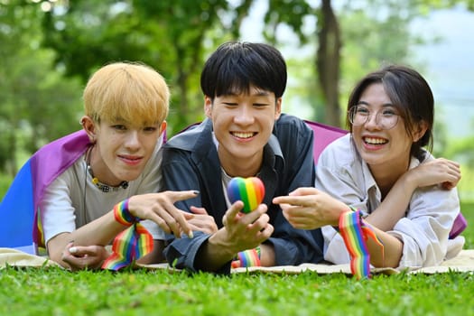 Young LGBT friends with rainbow heart celebrating gay pride, enjoying outdoor activities at the park. LGBT community concept.