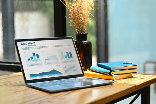 Laptop with financial diagrams graphs on wooden working desk. Business, finance and technology concept.