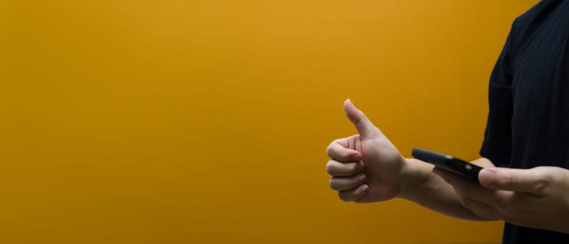 Man holding smartphone and showing thumb up isolated on yellow background with copy space for text.