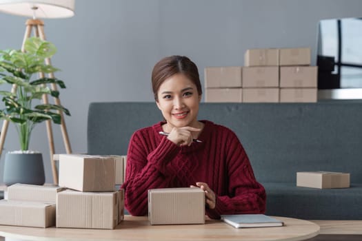 Asian Women business owner working at home with packing box on workplace - online shopping SME entrepreneur or online selling concept.