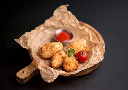 chicken fillet fried in batter with sauce on a wooden board on a black background