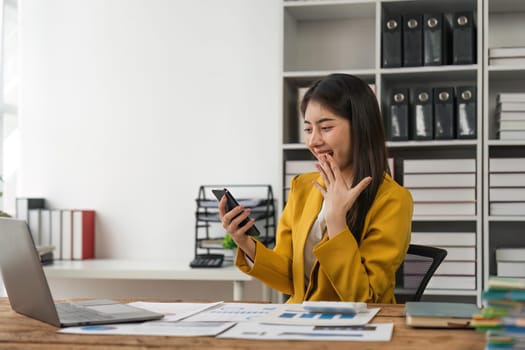 Excited businesswoman winning after achievement reading a smart phone sitting in a desk at office.