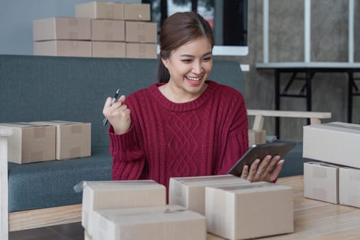 Happy young Asian woman entrepreneur, Smile for sales success after checking order from online shopping store in a tablet at home office, Concept of merchant business online and eCommerce.