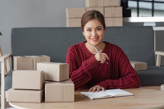 Asian Women business owner working at home with packing box on workplace - online shopping SME entrepreneur or online selling concept.