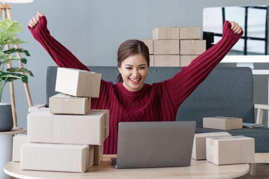 Happy young Asian woman entrepreneur, Smile for sales success after checking order from online shopping store in a laptop at home office, Concept of merchant business online and eCommerce.