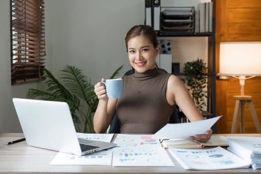 Young woman enjoying her coffee while working or studying on laptop computer at home.