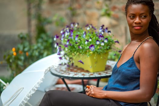 relaxed young black woman sitting. Stylish model. Braid dreadlock hairstyle. Confident African female in selective focus outdoors, fashion style, happiness concept. Outdoors.