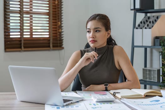 Young pretty asian using laptop with household expenses and financial document on table, work at home concept.